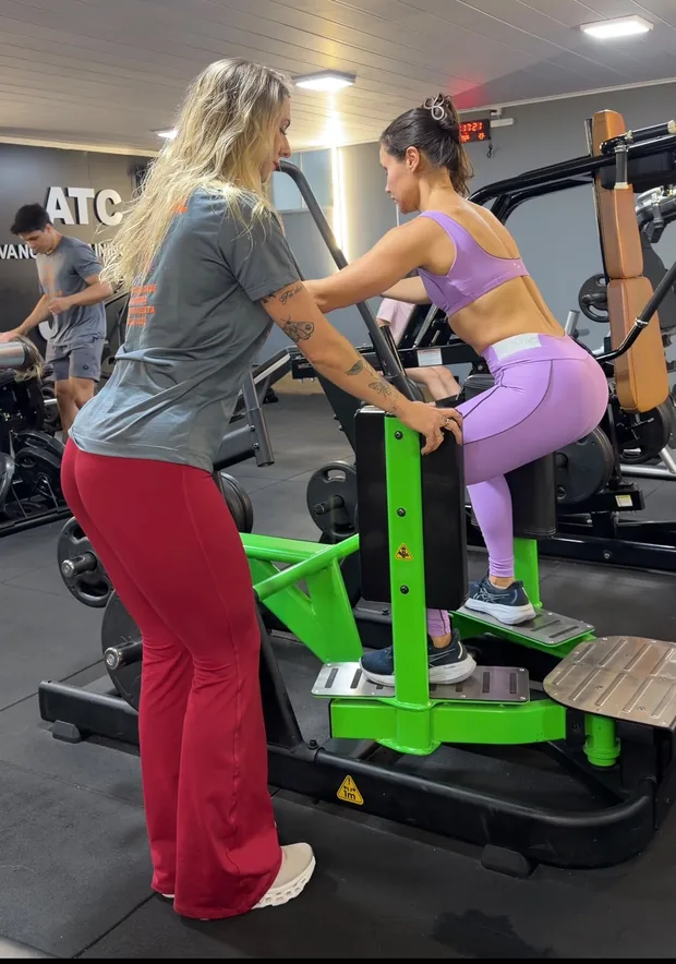 Flávia Pirchiner orientando a execução de um exercício ao lado de uma aluna na academia