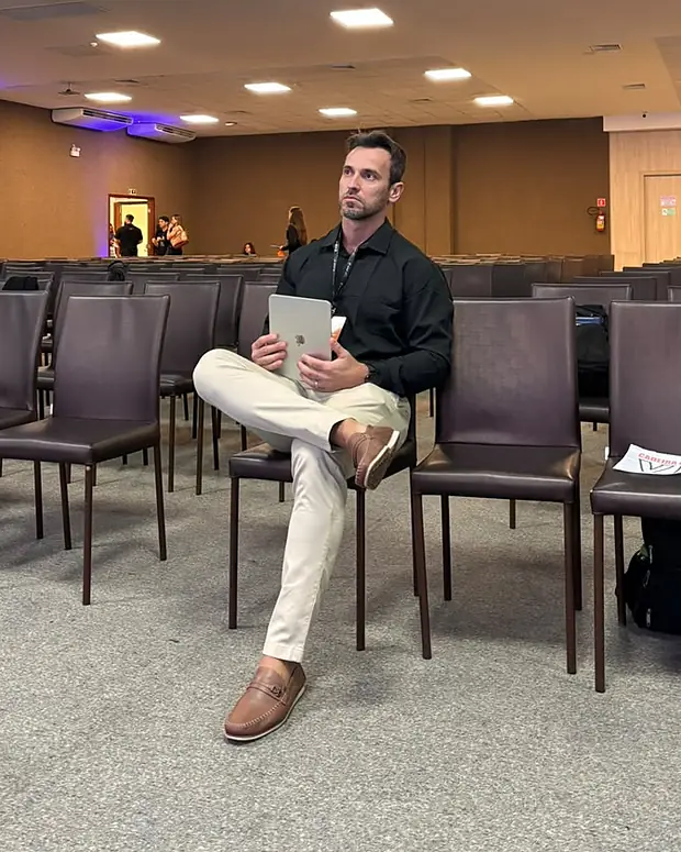 Dr. Victor Curty sentado no auditório de um congresso, com um tablet nas mãos, acompanhando as apresentações